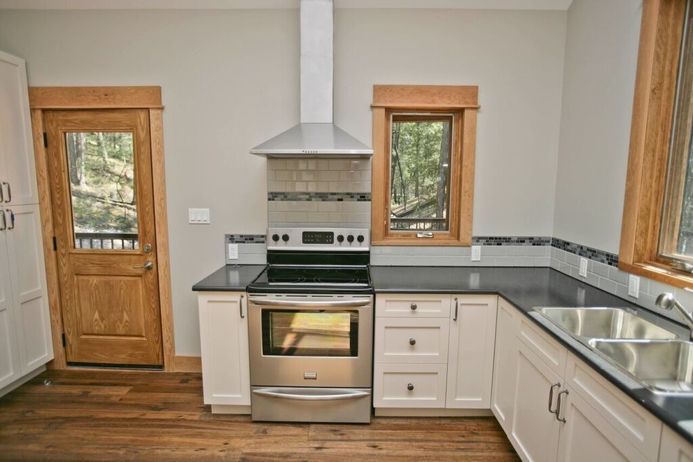Photo of a mid-sized arts and crafts l-shaped separate kitchen in Vancouver with a double-bowl sink, granite benchtops, white splashback, timber splashback, stainless steel appliances, dark hardwood floors, shaker cabinets, white cabinets and brown floor.