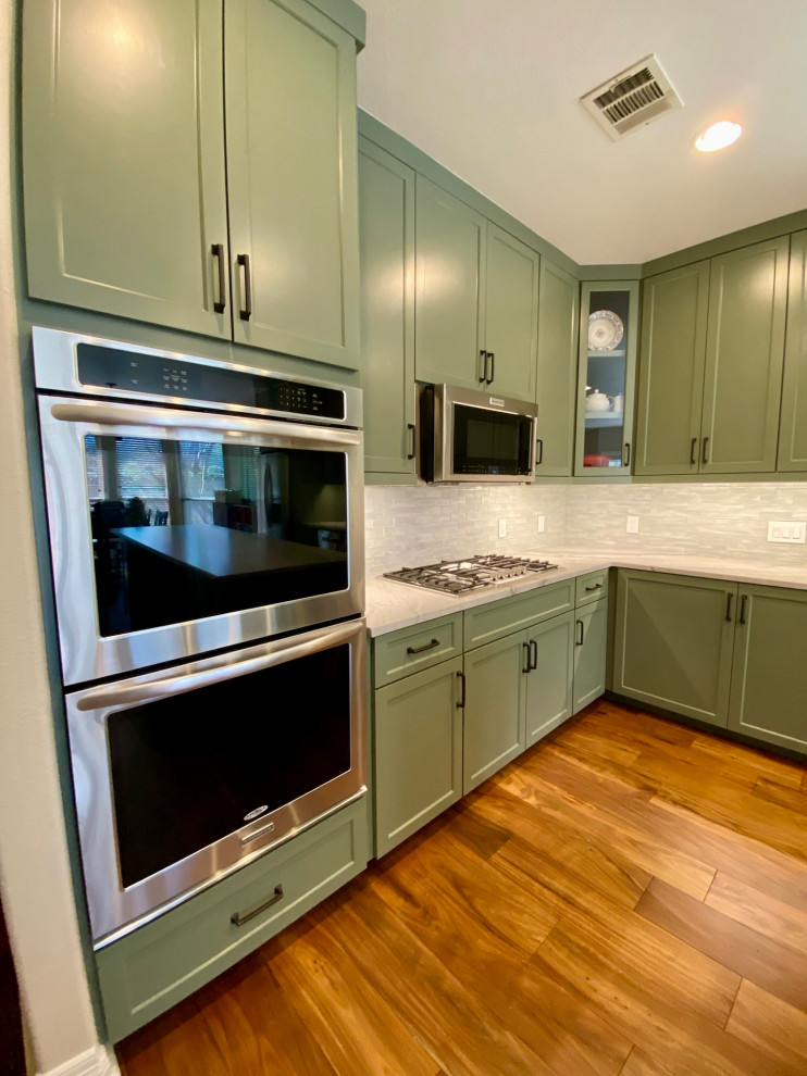 Foto på ett stort 60 tals vit kök, med en rustik diskho, luckor med infälld panel, gröna skåp, bänkskiva i kvartsit, vitt stänkskydd, stänkskydd i glaskakel, rostfria vitvaror, mellanmörkt trägolv, en köksö och brunt golv