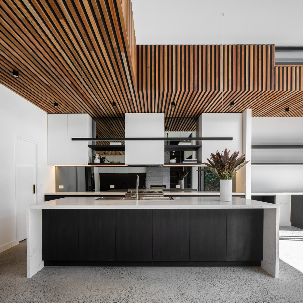 Large contemporary galley open plan kitchen in Melbourne with flat-panel cabinets, mirror splashback, stainless steel appliances, concrete floors, with island, grey floor, grey benchtop, a double-bowl sink, solid surface benchtops and grey splashback.
