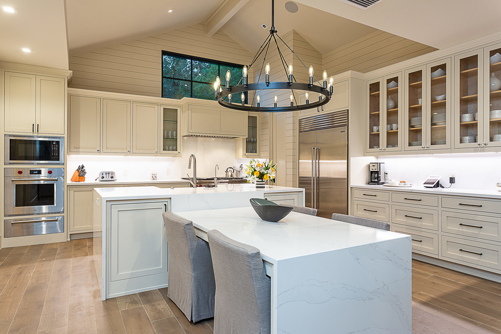 Inspiration for a large country l-shaped separate kitchen in Austin with a farmhouse sink, shaker cabinets, beige cabinets, marble benchtops, stainless steel appliances, medium hardwood floors, with island, brown floor and white benchtop.