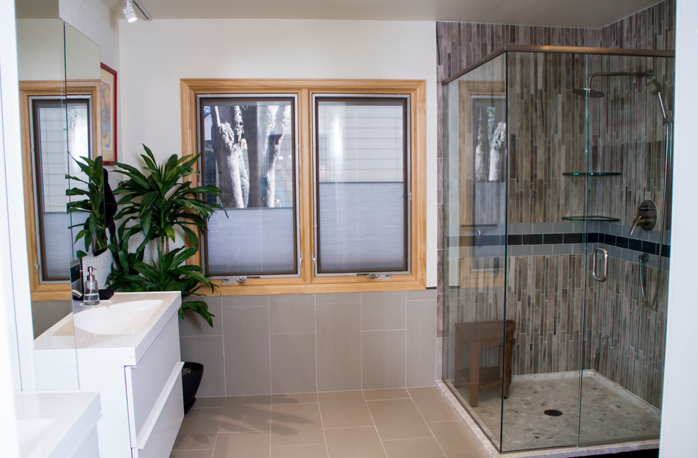 This is an example of a large transitional master bathroom in Denver with flat-panel cabinets, white cabinets, a corner shower, a two-piece toilet, porcelain tile, an integrated sink, multi-coloured tile, beige walls and porcelain floors.