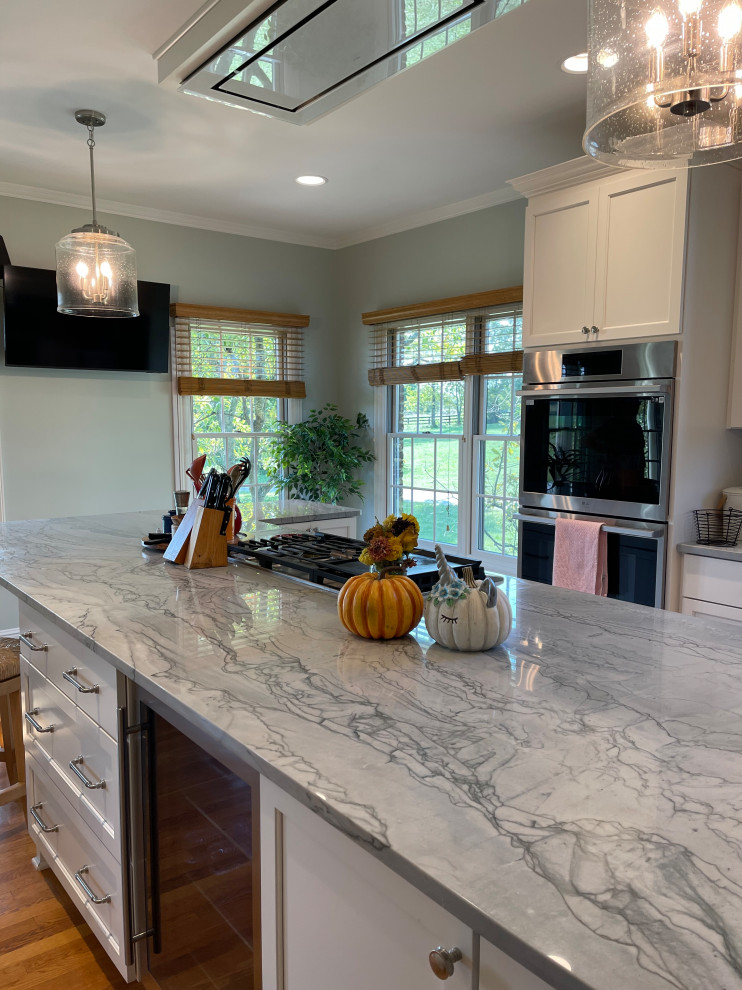 Large transitional light wood floor and brown floor eat-in kitchen photo with an undermount sink, shaker cabinets, white cabinets, quartzite countertops, green backsplash, marble backsplash, stainless steel appliances, an island and gray countertops
