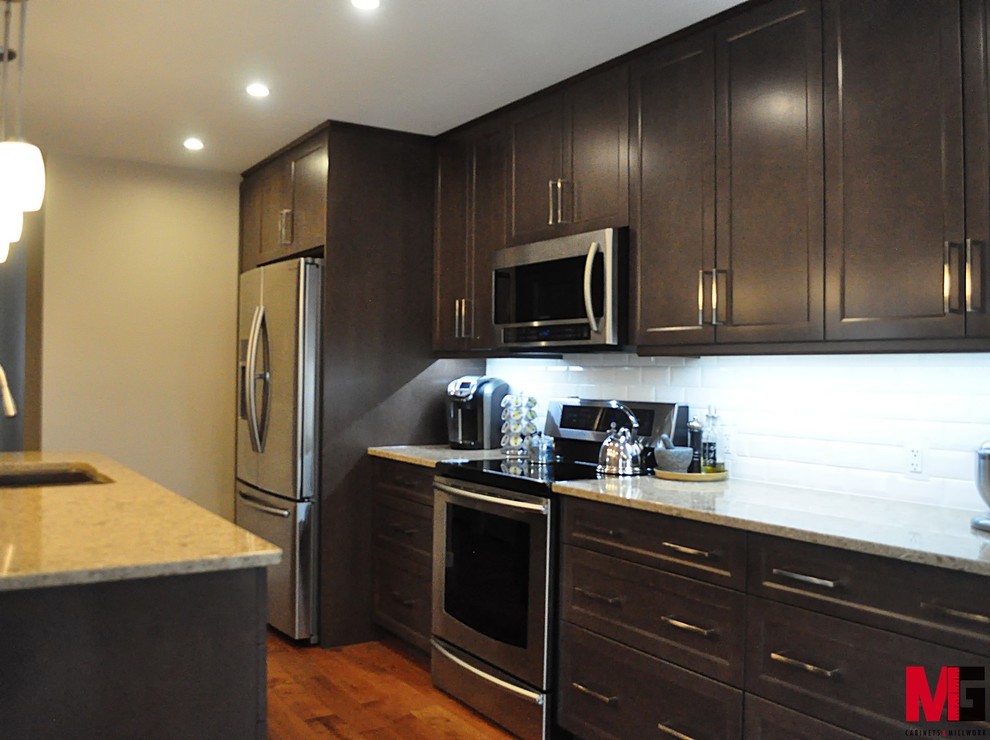Large transitional u-shaped medium tone wood floor and brown floor enclosed kitchen photo with an undermount sink, shaker cabinets, dark wood cabinets, granite countertops, white backsplash, subway tile backsplash, stainless steel appliances and an island