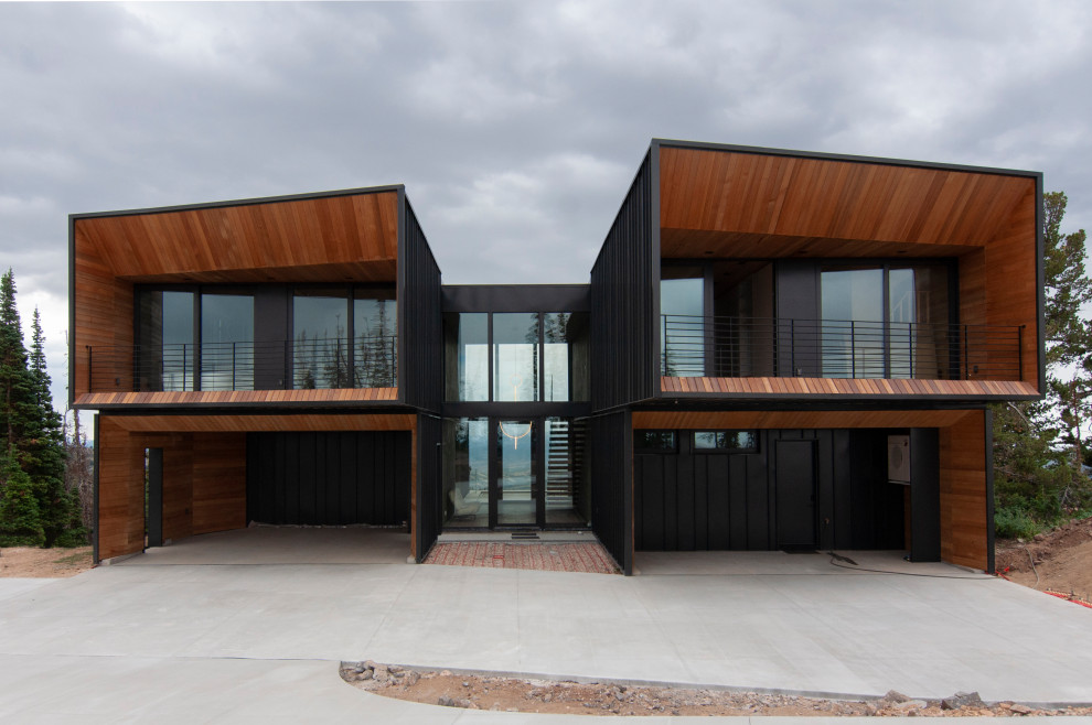 Стильный дизайн: двухэтажный, черный частный загородный дом в стиле модернизм с облицовкой из металла, односкатной крышей, металлической крышей, черной крышей, отделкой доской с нащельником и входной группой - последний тренд