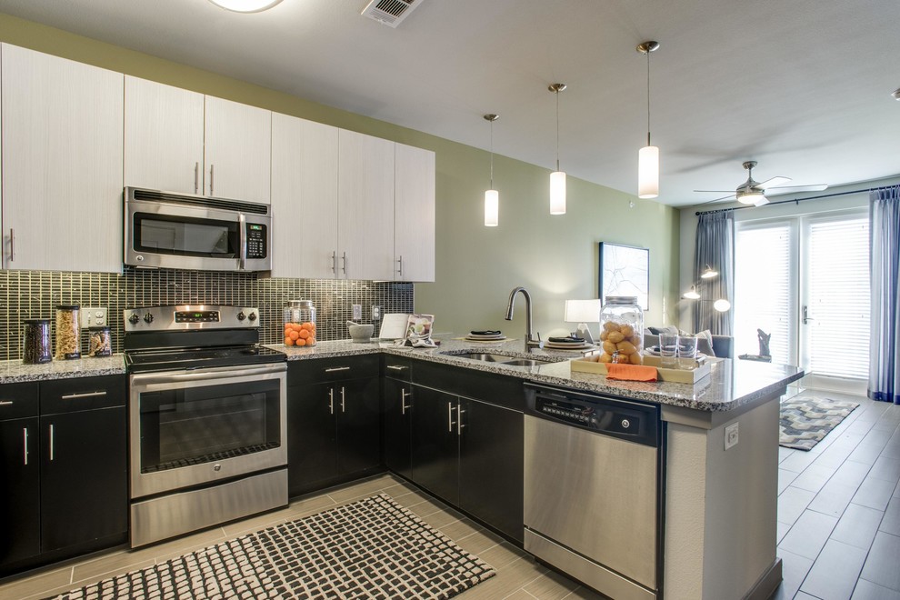 Example of a mid-sized transitional l-shaped porcelain tile and gray floor open concept kitchen design in Houston with a double-bowl sink, flat-panel cabinets, black cabinets, granite countertops, black backsplash, mosaic tile backsplash, stainless steel appliances and a peninsula