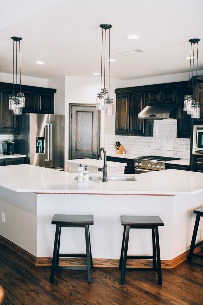 Design ideas for a mid-sized transitional l-shaped eat-in kitchen in Dallas with an undermount sink, raised-panel cabinets, black cabinets, quartzite benchtops, white splashback, subway tile splashback, stainless steel appliances, medium hardwood floors, with island and brown floor.
