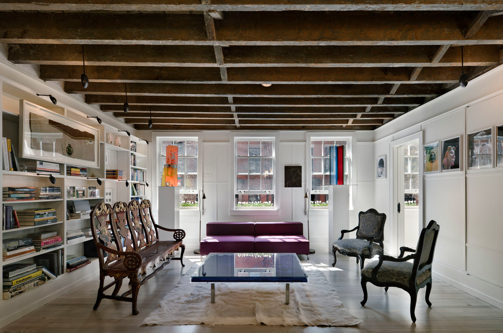 Photo of an industrial family room in New York with a library, white walls and light hardwood floors.