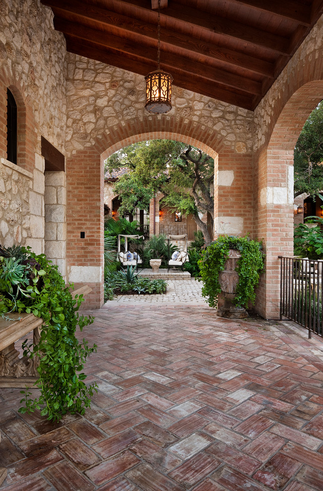 Photo of a large mediterranean side yard patio in Austin with brick pavers and a roof extension.