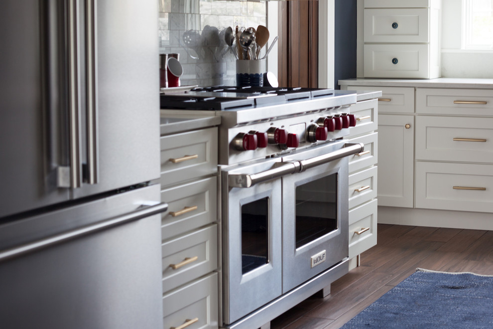 Inspiration for a large transitional l-shaped enclosed kitchen remodel in Boston with a farmhouse sink, shaker cabinets, white cabinets, quartz countertops, white backsplash, stainless steel appliances, an island and white countertops