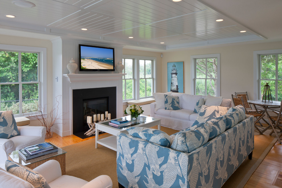 Photo of a mid-sized beach style open concept living room in Boston with a standard fireplace, a wall-mounted tv, beige walls, light hardwood floors, a metal fireplace surround and brown floor.
