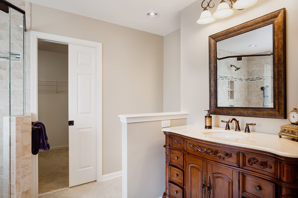 Mid-sized traditional master bathroom in Charlotte with furniture-like cabinets, brown cabinets, a curbless shower, a two-piece toilet, beige tile, porcelain tile, beige walls, plywood floors, an undermount sink, marble benchtops, beige floor and a hinged shower door.