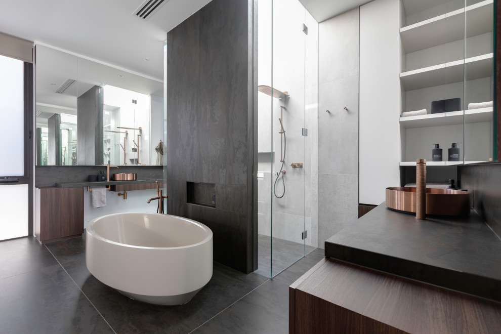Design ideas for a large contemporary master bathroom in Melbourne with stone tile, a hinged shower door, flat-panel cabinets, dark wood cabinets, a freestanding tub, a curbless shower, gray tile, a vessel sink, grey floor and black benchtops.