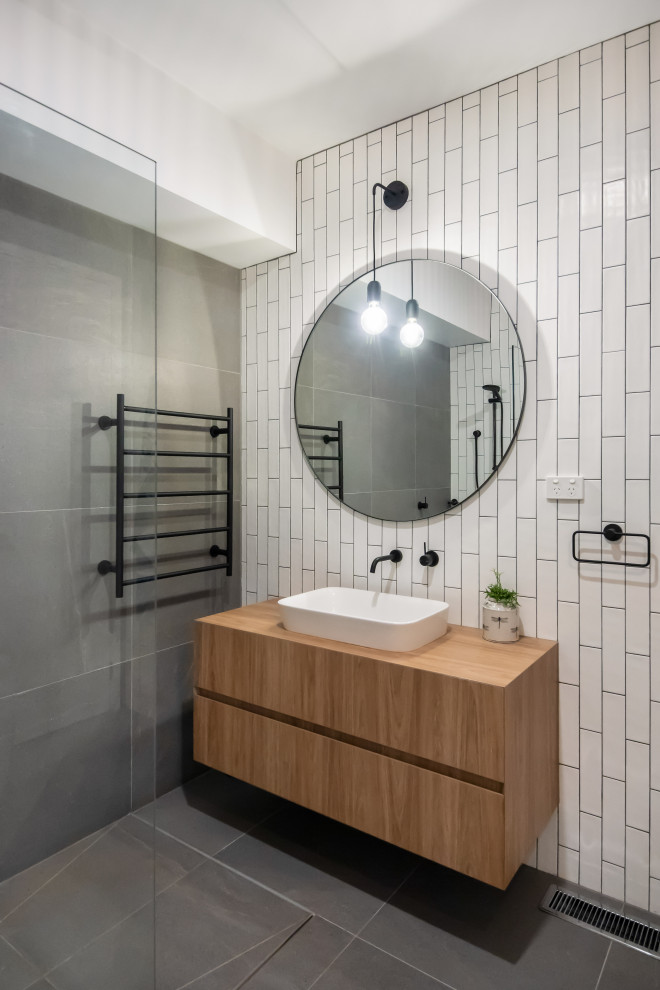 Large contemporary master bathroom in Melbourne with furniture-like cabinets, medium wood cabinets, a freestanding tub, an open shower, a one-piece toilet, white tile, subway tile, white walls, porcelain floors, a drop-in sink, laminate benchtops and grey floor.