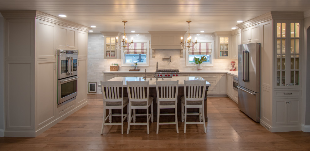 Inspiration for a transitional medium tone wood floor, brown floor and shiplap ceiling eat-in kitchen remodel with a farmhouse sink, shaker cabinets, beige cabinets, quartz countertops, white backsplash, cement tile backsplash, stainless steel appliances, an island and white countertops