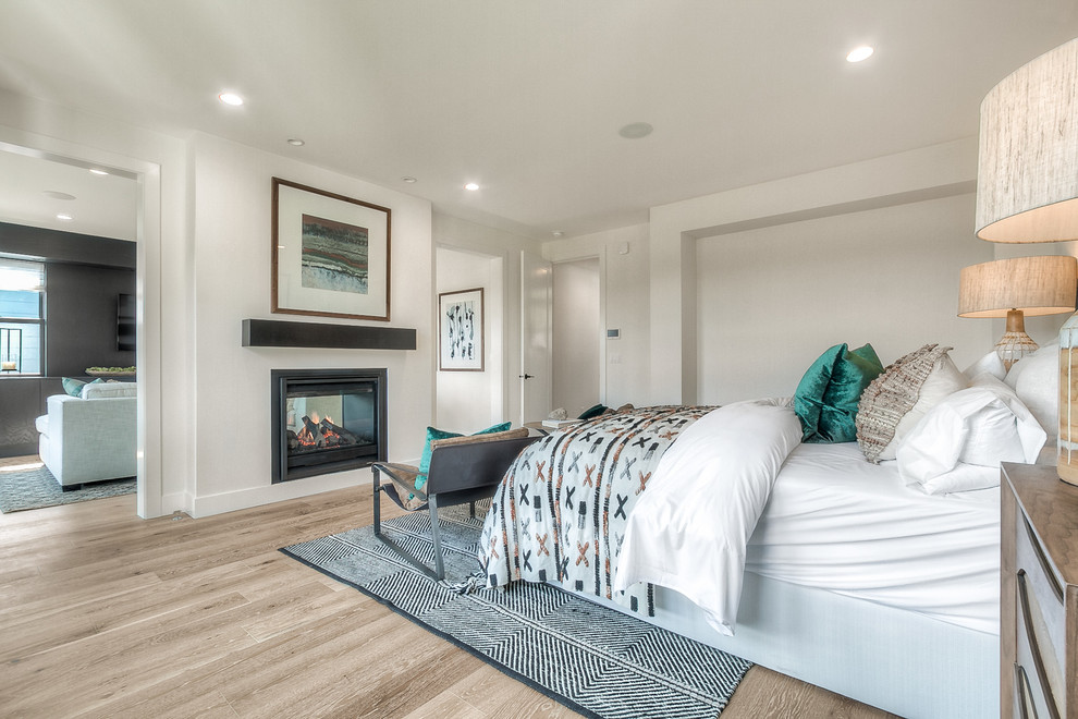 This is an example of a transitional master bedroom in Seattle with white walls, light hardwood floors and a two-sided fireplace.