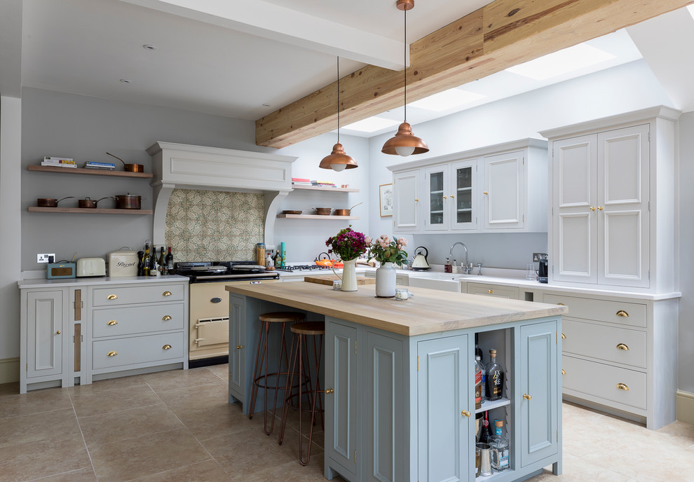 Photo of a mid-sized country l-shaped eat-in kitchen in London with a farmhouse sink, shaker cabinets, grey cabinets, solid surface benchtops, green splashback, porcelain splashback, stainless steel appliances, limestone floors, with island and beige floor.
