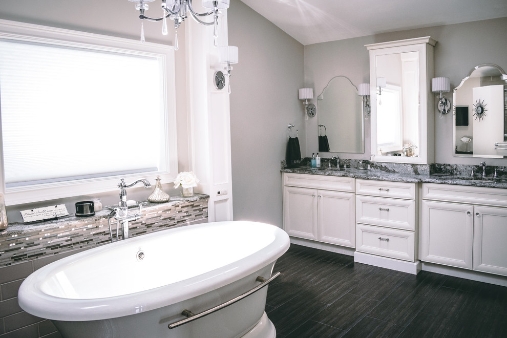 Example of a transitional brown tile and glass tile dark wood floor and brown floor freestanding bathtub design in New York with recessed-panel cabinets, white cabinets, a two-piece toilet, gray walls, an undermount sink, granite countertops, a hinged shower door and multicolored countertops