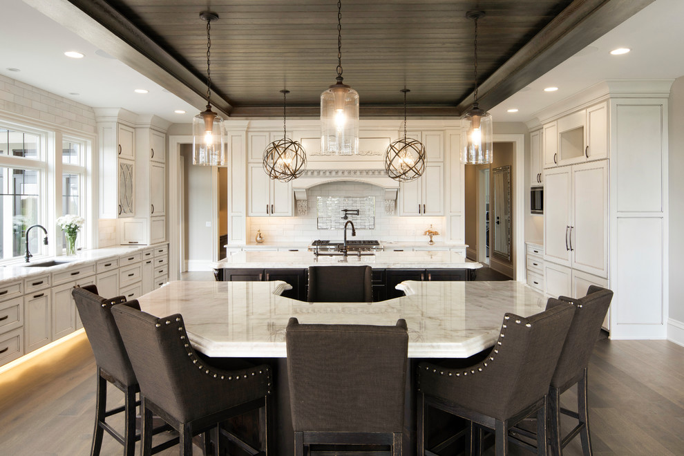Expansive traditional u-shaped eat-in kitchen in Minneapolis with an undermount sink, raised-panel cabinets, white cabinets, solid surface benchtops, white splashback, ceramic splashback, panelled appliances, medium hardwood floors, multiple islands and white benchtop.