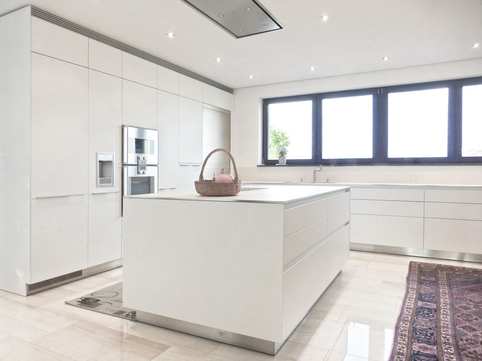 Exempel på ett stort modernt grå grått kök, med en nedsänkt diskho, släta luckor, vita skåp, bänkskiva i rostfritt stål, vitt stänkskydd, fönster som stänkskydd, integrerade vitvaror, kalkstensgolv, en köksö och beiget golv