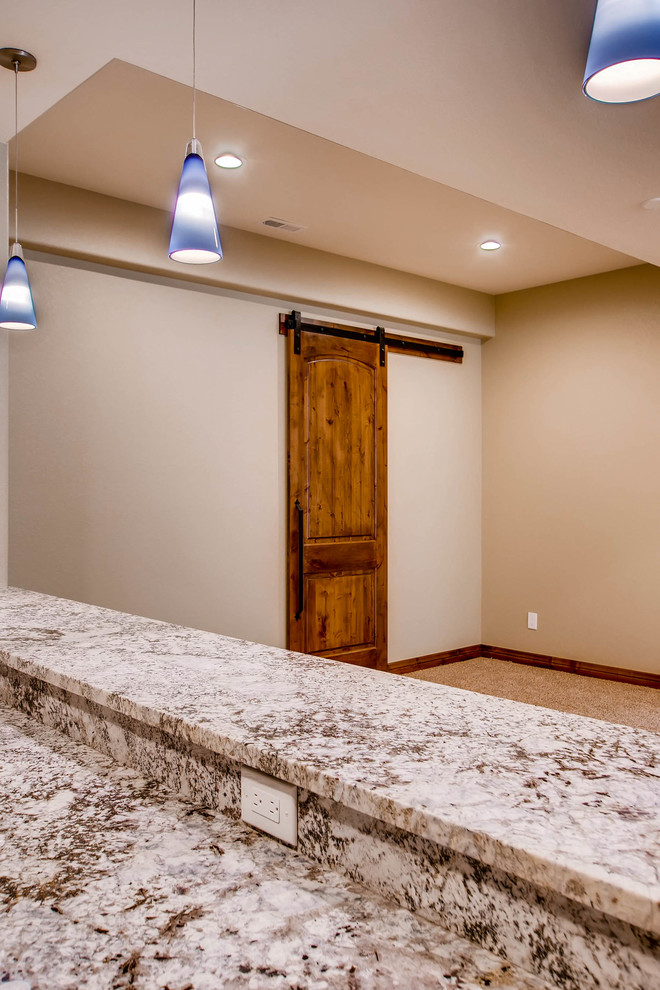 Expansive traditional fully buried basement in Denver with beige walls, carpet, a standard fireplace, a stone fireplace surround and beige floor.