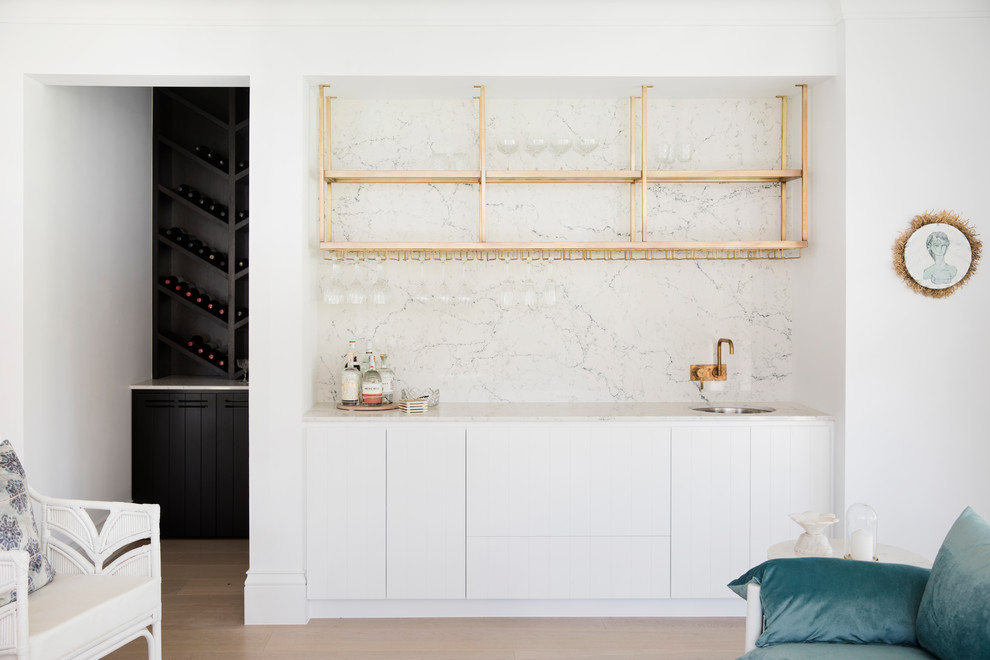Mid-sized beach style single-wall wet bar in Sydney with an undermount sink, white cabinets, white splashback and white benchtop.