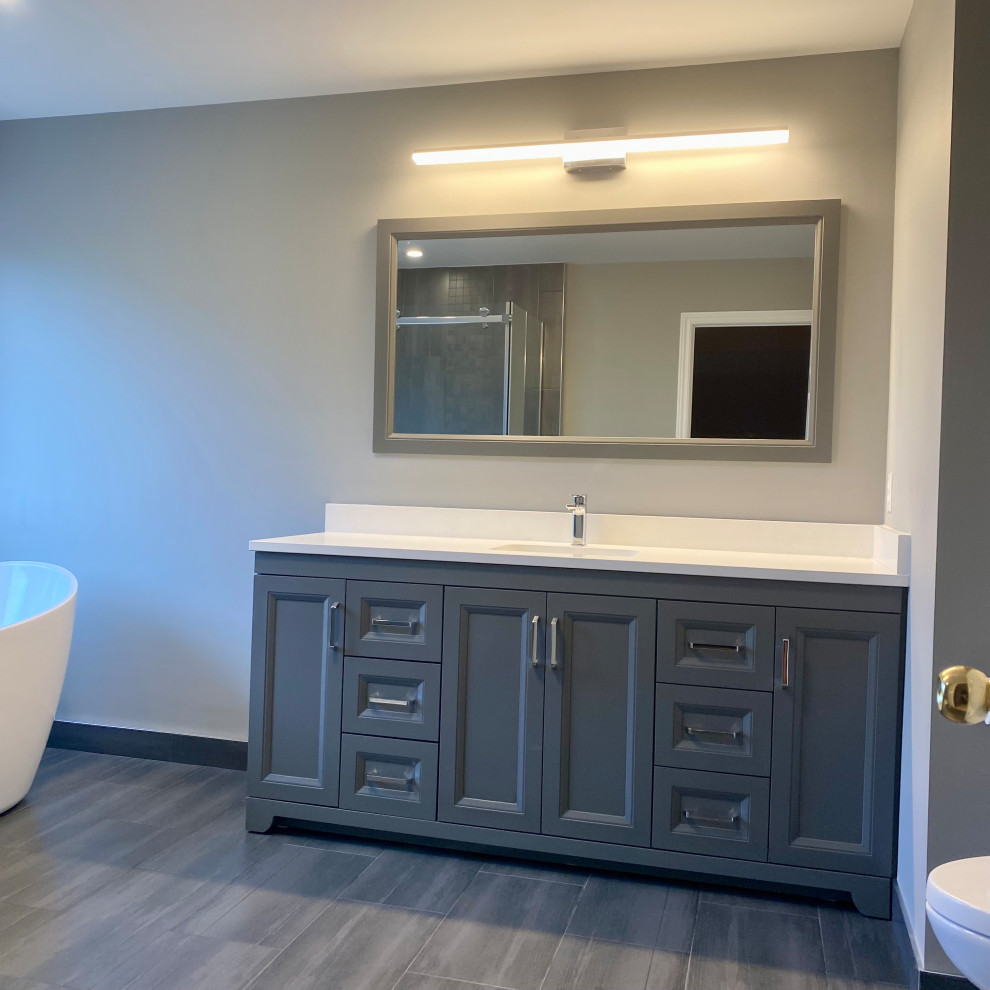 Example of a huge transitional master porcelain tile porcelain tile, gray floor and single-sink freestanding bathtub design with recessed-panel cabinets, a one-piece toilet, an undermount sink, quartzite countertops, white countertops and a built-in vanity
