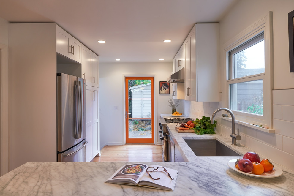 Contemporary kitchen in Seattle with shaker cabinets, marble benchtops, white splashback, ceramic splashback, stainless steel appliances and medium hardwood floors.