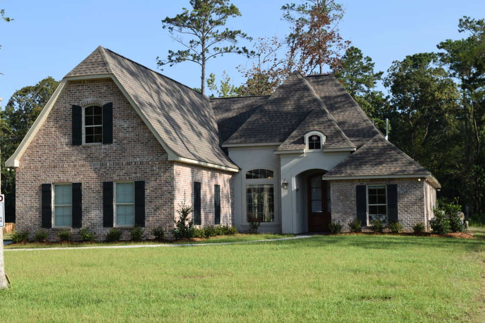 This is an example of a large traditional two-storey brick beige house exterior in New Orleans with a shingle roof.