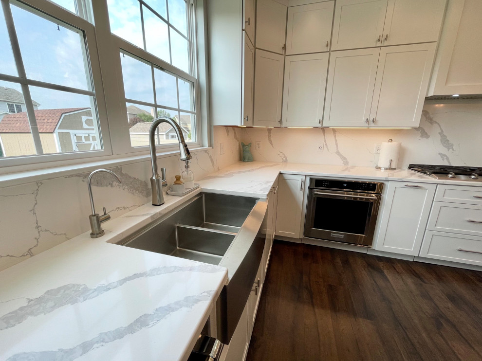 Inspiration for a large transitional u-shaped medium tone wood floor and brown floor eat-in kitchen remodel in Chicago with a farmhouse sink, shaker cabinets, white cabinets, quartz countertops, white backsplash, quartz backsplash, stainless steel appliances, two islands and white countertops