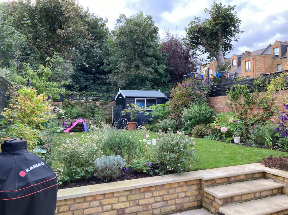 Kleiner Moderner Garten im Sommer, hinter dem Haus mit Blumenbeet, direkter Sonneneinstrahlung, Natursteinplatten und Holzzaun in London