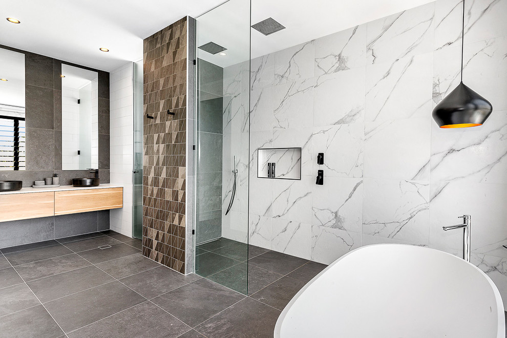 This is an example of a contemporary master bathroom in Brisbane with porcelain floors, grey floor, flat-panel cabinets, light wood cabinets, a freestanding tub, an open shower, marble, white walls, a vessel sink, an open shower and black and white tile.