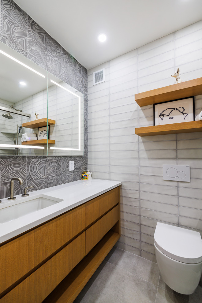 Mid-sized modern powder room in New York with furniture-like cabinets, brown cabinets, a wall-mount toilet, black and white tile, ceramic tile, grey walls, ceramic floors, an integrated sink, engineered quartz benchtops, grey floor, white benchtops and a built-in vanity.