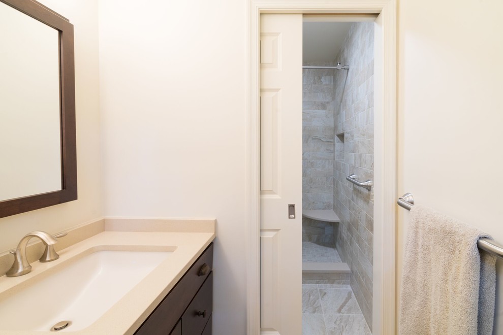 Inspiration for a mid-sized traditional 3/4 bathroom in Philadelphia with shaker cabinets, dark wood cabinets, an alcove shower, a two-piece toilet, beige tile, stone slab, beige walls, ceramic floors, an undermount sink, engineered quartz benchtops, grey floor and a sliding shower screen.