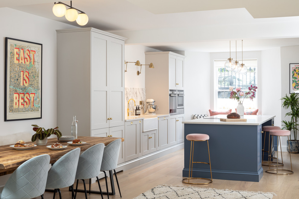 Large transitional open plan kitchen in London with a farmhouse sink, shaker cabinets, with island and white benchtop.