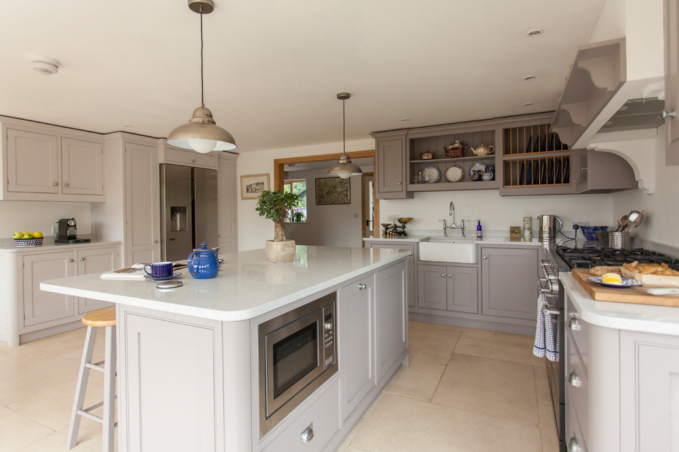 This is an example of a large traditional l-shaped eat-in kitchen in Gloucestershire with a farmhouse sink, shaker cabinets, grey cabinets, quartzite benchtops, stainless steel appliances, travertine floors, with island, beige floor and white benchtop.