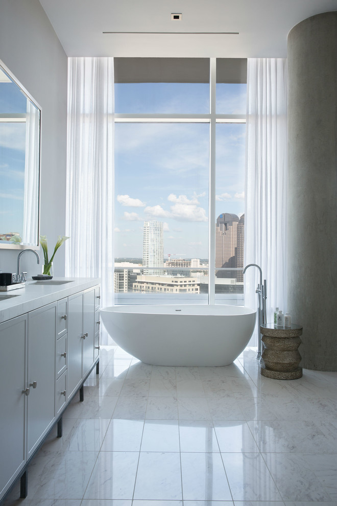This is an example of a modern master bathroom in Dallas with an undermount sink, recessed-panel cabinets, white cabinets, marble benchtops, a freestanding tub, white tile, white walls and marble floors.