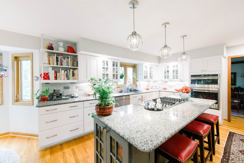 Photo of a large eclectic galley eat-in kitchen in Cincinnati with an undermount sink, shaker cabinets, grey cabinets, granite benchtops, grey splashback, subway tile splashback, stainless steel appliances, light hardwood floors, with island, brown floor and grey benchtop.
