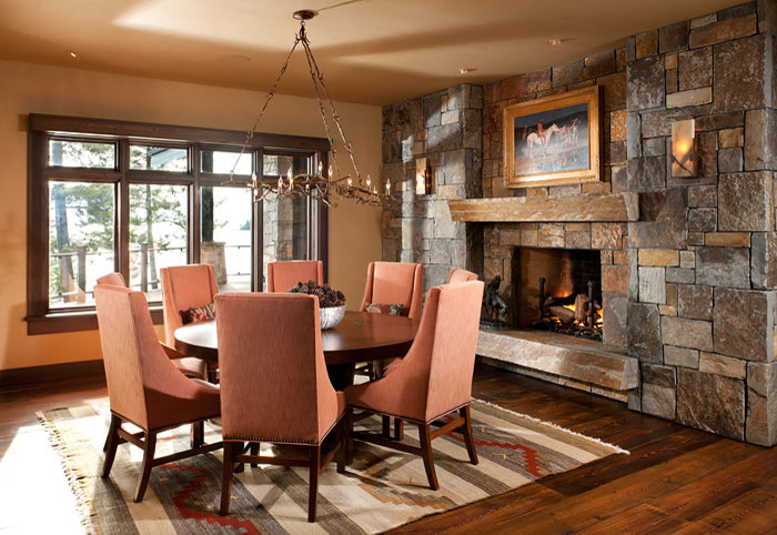 Mountain style medium tone wood floor kitchen/dining room combo photo with beige walls, a standard fireplace and a stone fireplace