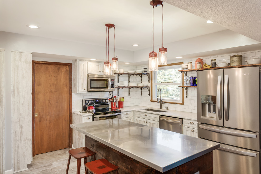 Photo of a mid-sized country l-shaped kitchen in Detroit with an undermount sink, shaker cabinets, light wood cabinets, white splashback, cement tile splashback, stainless steel appliances, painted wood floors, with island, grey floor, stainless steel benchtops and grey benchtop.