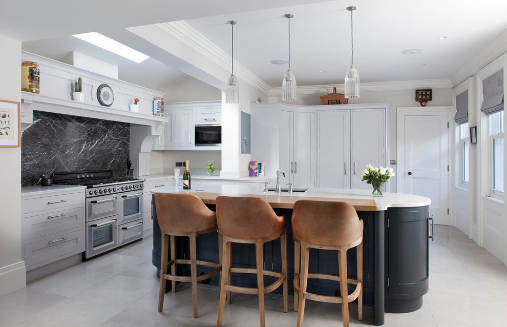 This is an example of a large contemporary u-shaped eat-in kitchen in Belfast with shaker cabinets, blue cabinets, marble benchtops, black splashback, stone slab splashback, porcelain floors, with island, an undermount sink and stainless steel appliances.