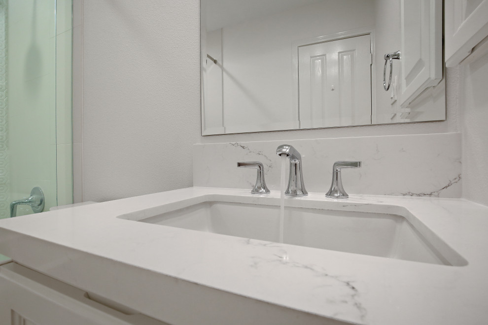 This is an example of a small transitional kids bathroom in Houston with raised-panel cabinets, white cabinets, an alcove tub, a shower/bathtub combo, a two-piece toilet, white tile, porcelain tile, white walls, ceramic floors, an undermount sink, engineered quartz benchtops, white floor, a sliding shower screen and white benchtops.