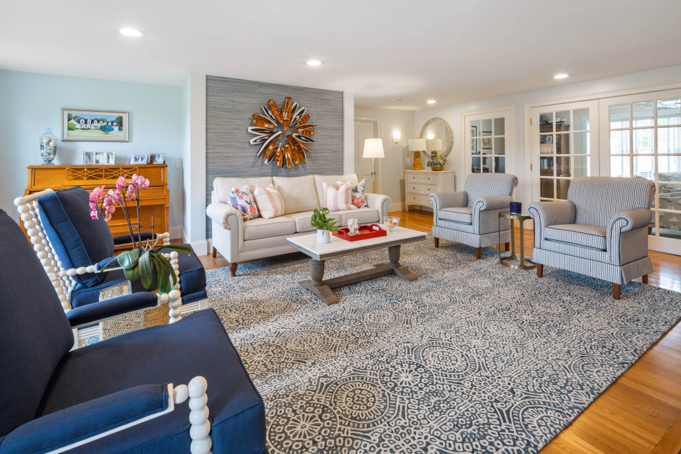Photo of a large beach style open concept living room in Boston with blue walls, medium hardwood floors, a standard fireplace, no tv, brown floor and wallpaper.