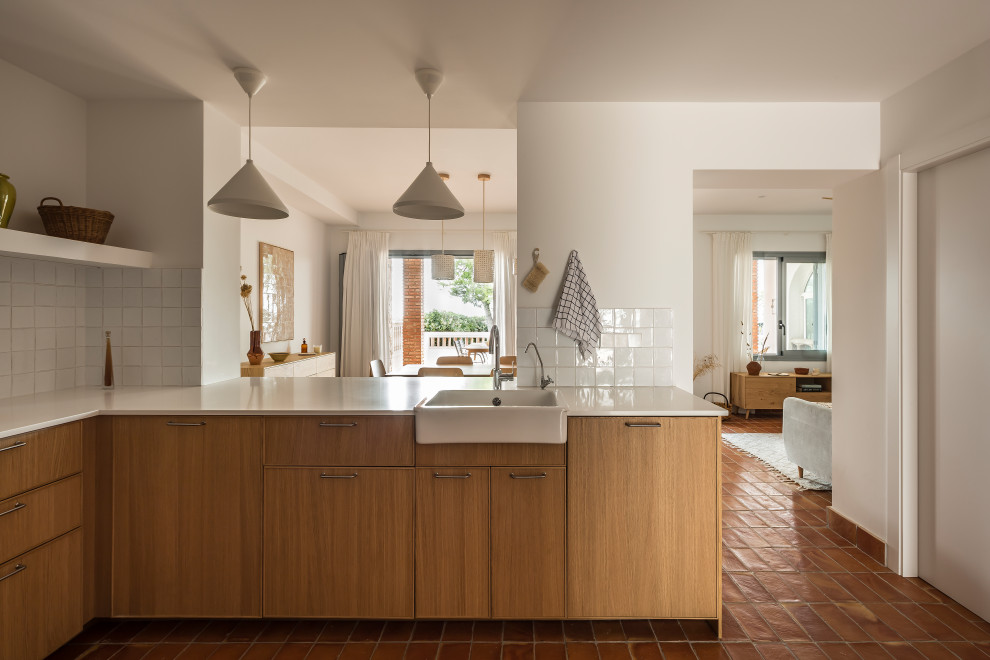 This is an example of a small mediterranean u-shaped eat-in kitchen in Valencia with a drop-in sink, flat-panel cabinets, brown cabinets, quartz benchtops, white splashback, terra-cotta splashback, stainless steel appliances, terra-cotta floors, brown floor and beige benchtop.