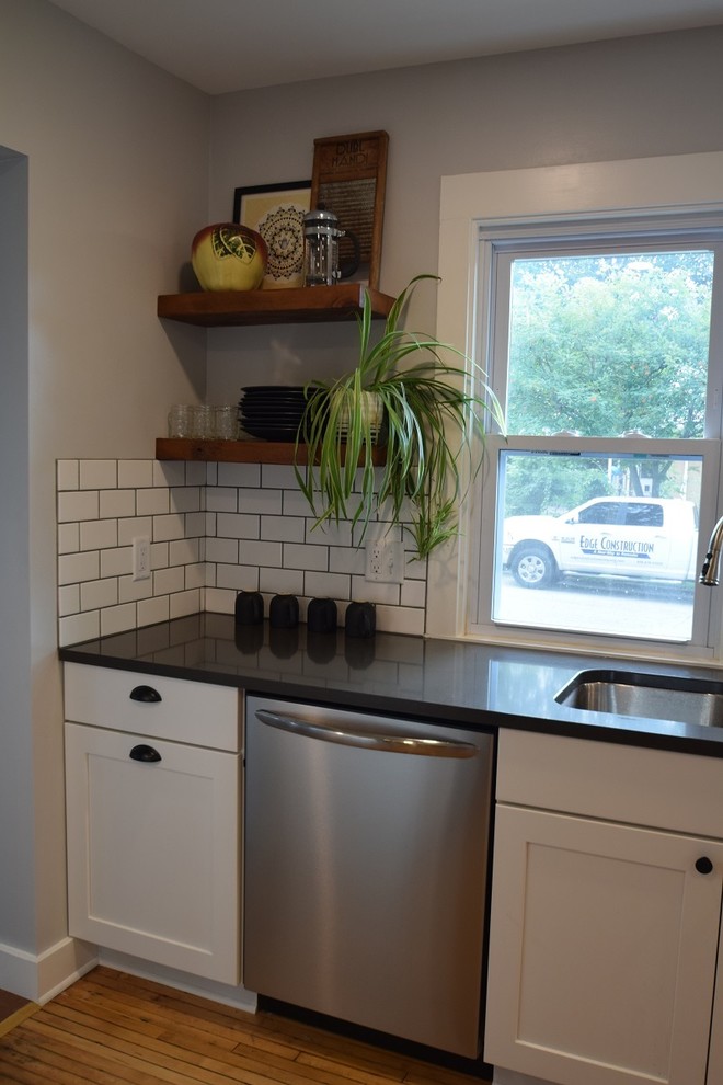 Kitchen - transitional u-shaped light wood floor kitchen idea with an undermount sink, shaker cabinets, white cabinets, quartz countertops, white backsplash, subway tile backsplash, stainless steel appliances, no island and black countertops