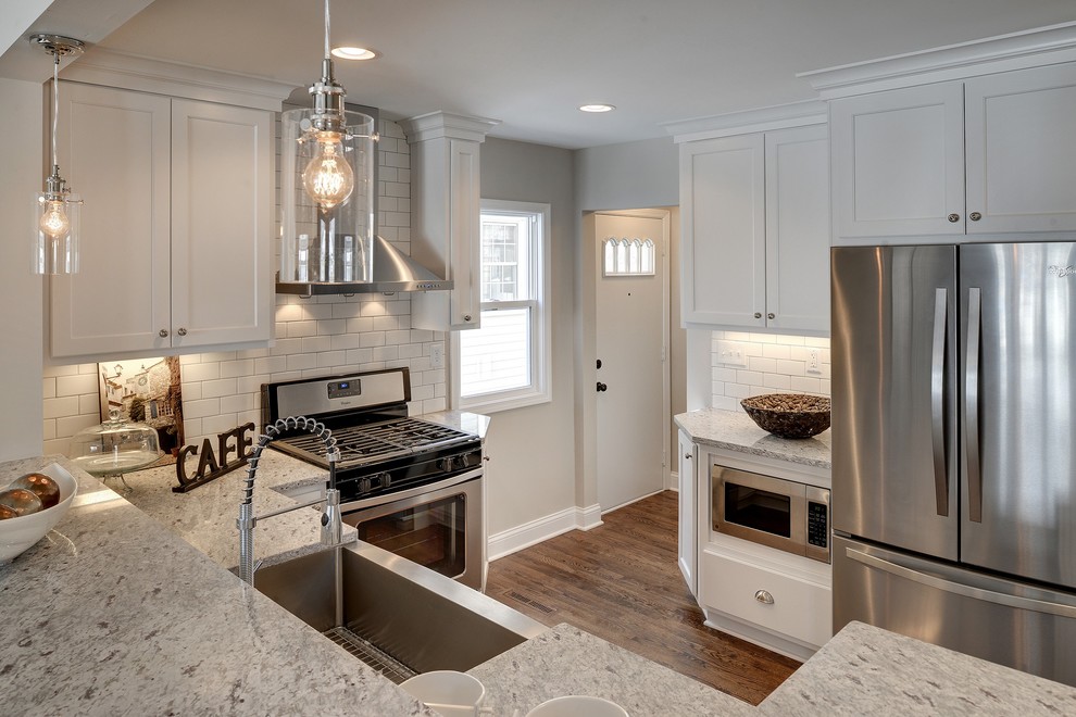 Example of a small transitional l-shaped medium tone wood floor eat-in kitchen design in Minneapolis with a farmhouse sink, flat-panel cabinets, white cabinets, granite countertops, white backsplash, ceramic backsplash and stainless steel appliances
