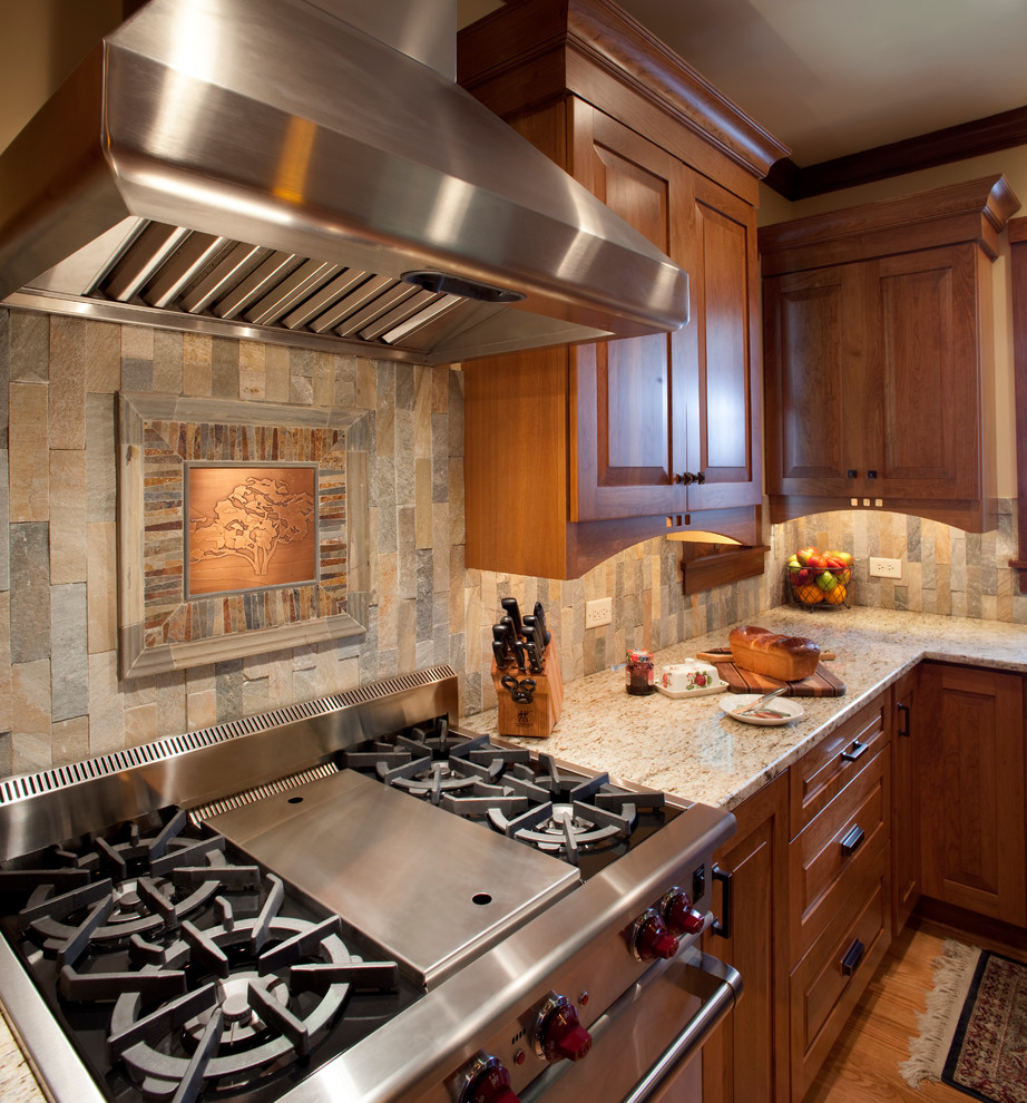 Inspiration for a mid-sized arts and crafts l-shaped eat-in kitchen in Chicago with with island, granite benchtops, stainless steel appliances, a double-bowl sink, raised-panel cabinets, medium wood cabinets, multi-coloured splashback, stone tile splashback and light hardwood floors.