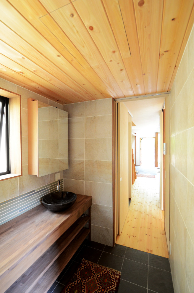 Пример оригинального дизайна: маленький туалет в скандинавском стиле с открытыми фасадами, коричневыми фасадами, бежевой плиткой, керамогранитной плиткой, бежевыми стенами, полом из керамогранита, накладной раковиной, столешницей из дерева, черным полом, коричневой столешницей, встроенной тумбой и деревянным потолком для на участке и в саду