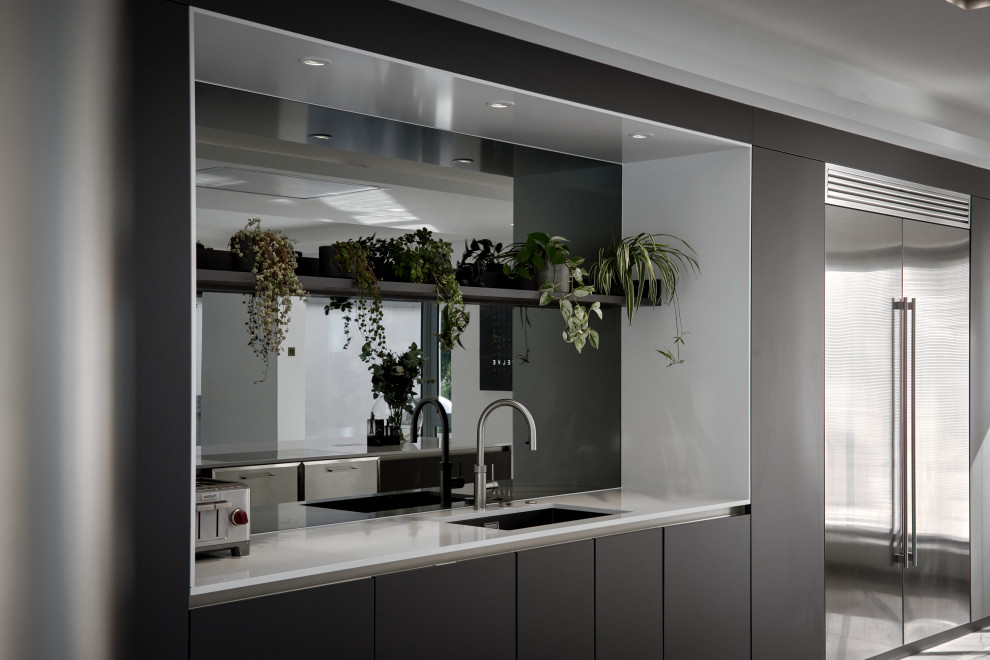 This is an example of a large contemporary single-wall open plan kitchen in Hampshire with a built-in sink, flat-panel cabinets, grey cabinets, engineered stone countertops, grey splashback, mirror splashback, stainless steel appliances, porcelain flooring, an island, white floors and white worktops.