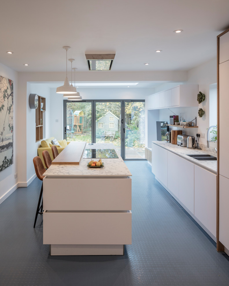 Photo of a contemporary galley kitchen in Gloucestershire with a submerged sink, flat-panel cabinets, white cabinets, integrated appliances, an island, grey floors and white worktops.