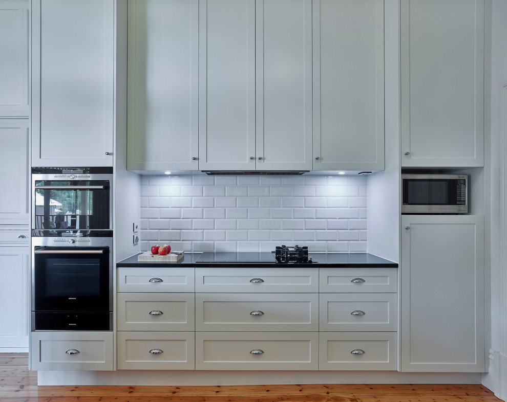 This is an example of a mid-sized contemporary l-shaped eat-in kitchen in Other with an undermount sink, shaker cabinets, white cabinets, granite benchtops, white splashback, subway tile splashback, stainless steel appliances and medium hardwood floors.